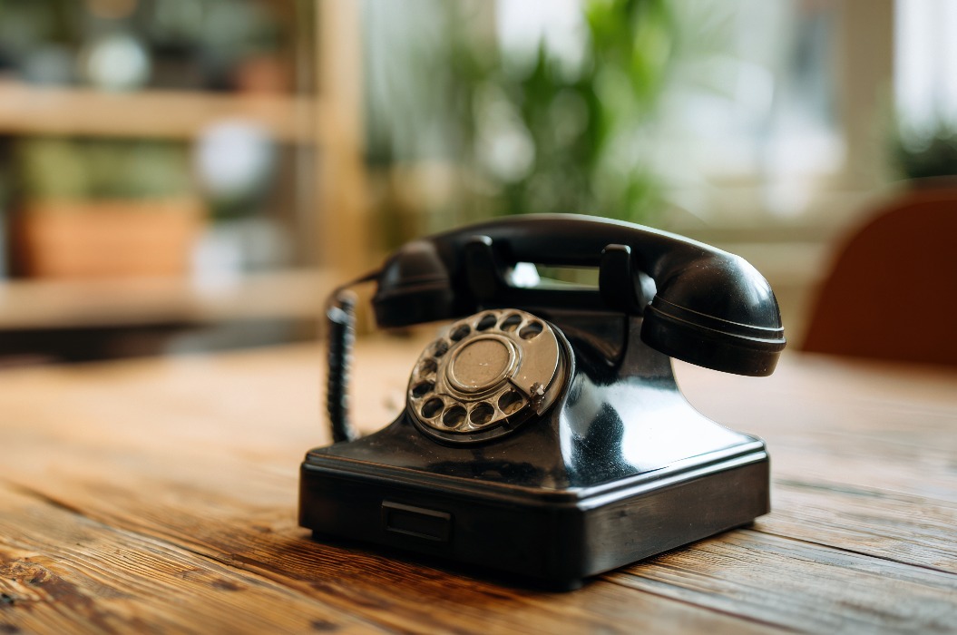 Ein schwarzes Vintage-Telefon mit Wählscheibe auf einem rustikalen Holztisch in einem Innenraum, das Retro-Kommunikation und klassisches Design in einer nostalgischen Atmosphäre präsentiert