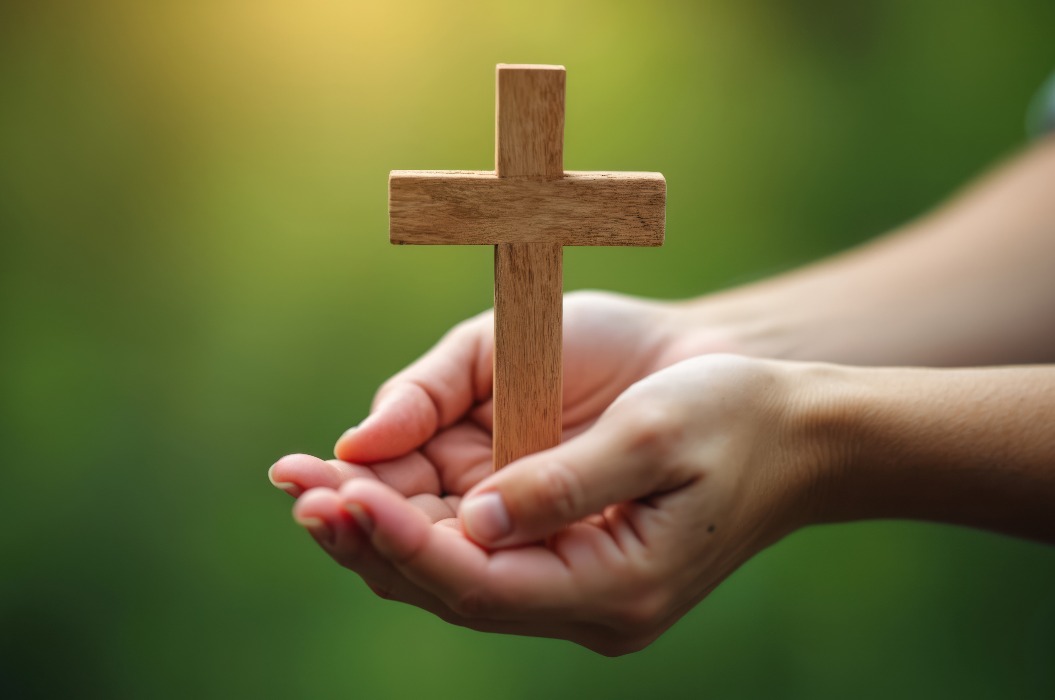 Hände, die sanft ein Holzkreuz umschließen. Symbol für Glauben, Hingabe und Ehrfurcht. Begriffe wie Spiritualität, Gebet, Hoffnung, Frieden und Christentum. Religion, Glaube, Gottesdienst, Spiritualität, Dankbarkeit, Besinnung.